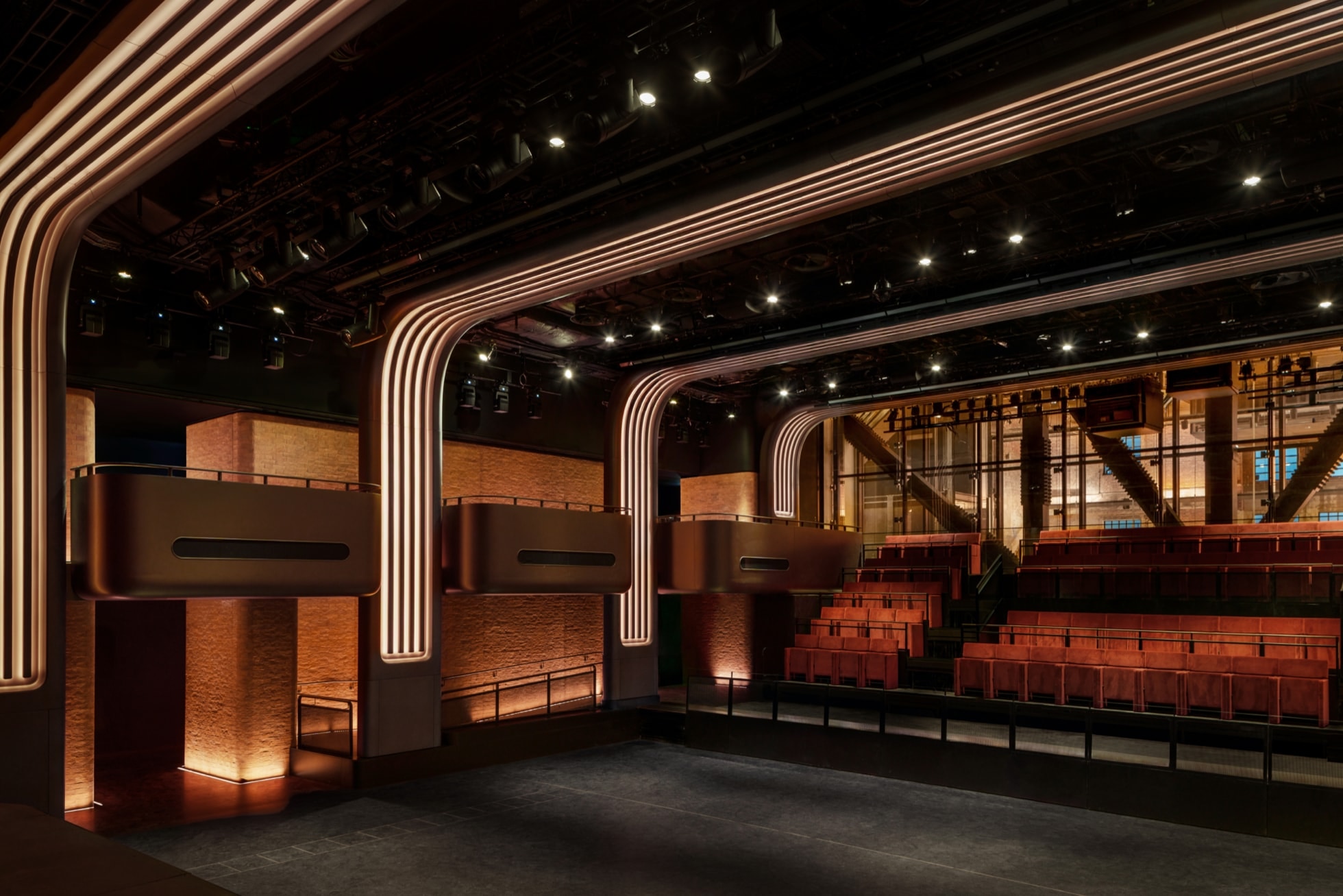 The performance space inside Apple Music Hall, with brick walls, bronze balconies and seating under lit arches.