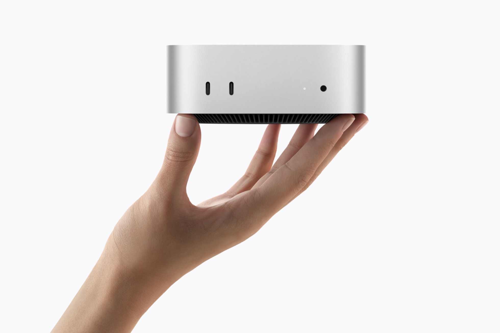 A person's hand holds the silver Mac mini, showing its front ports.